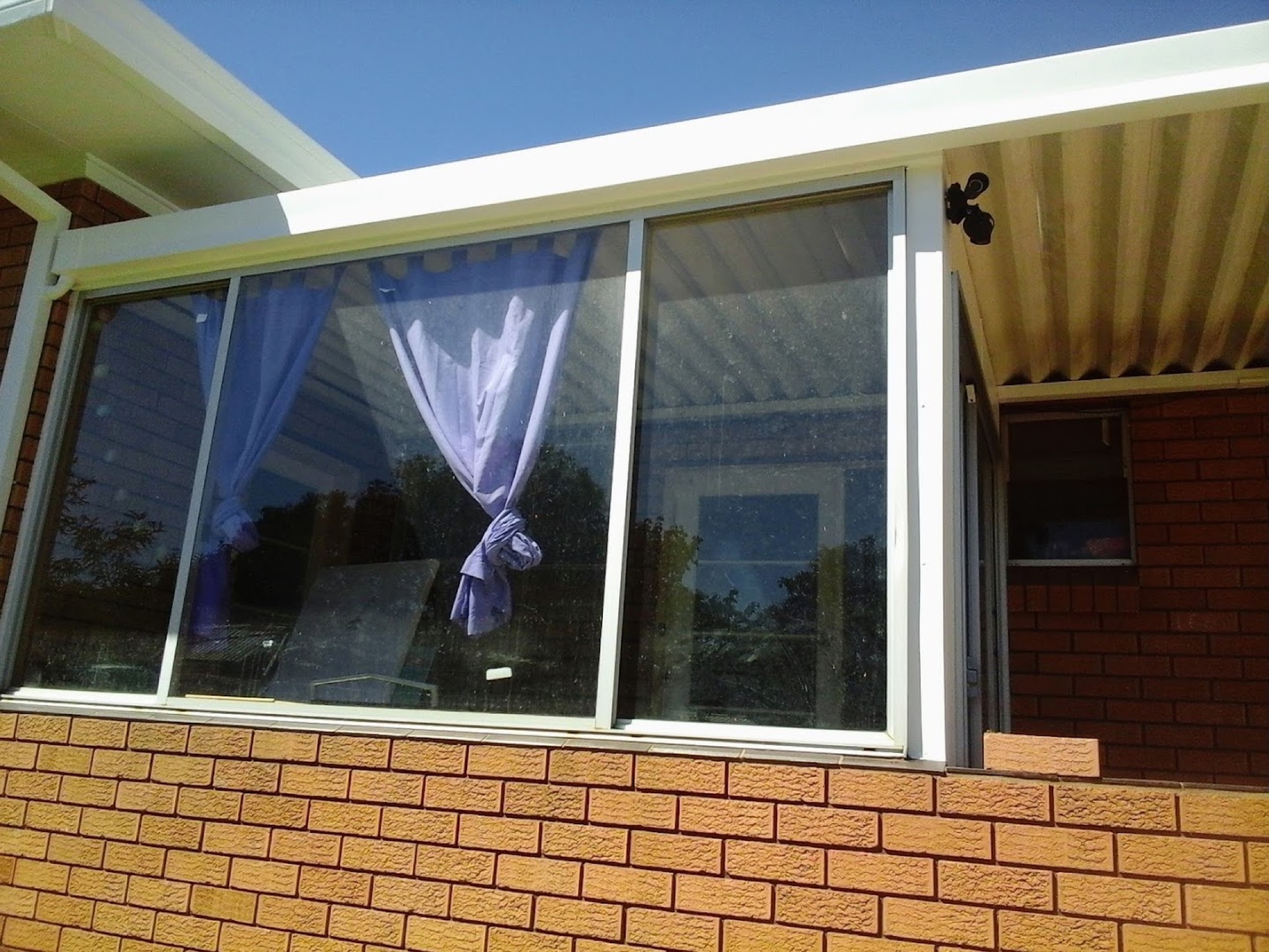 A brick house wall with a wide awning window under a corrugated patio roof