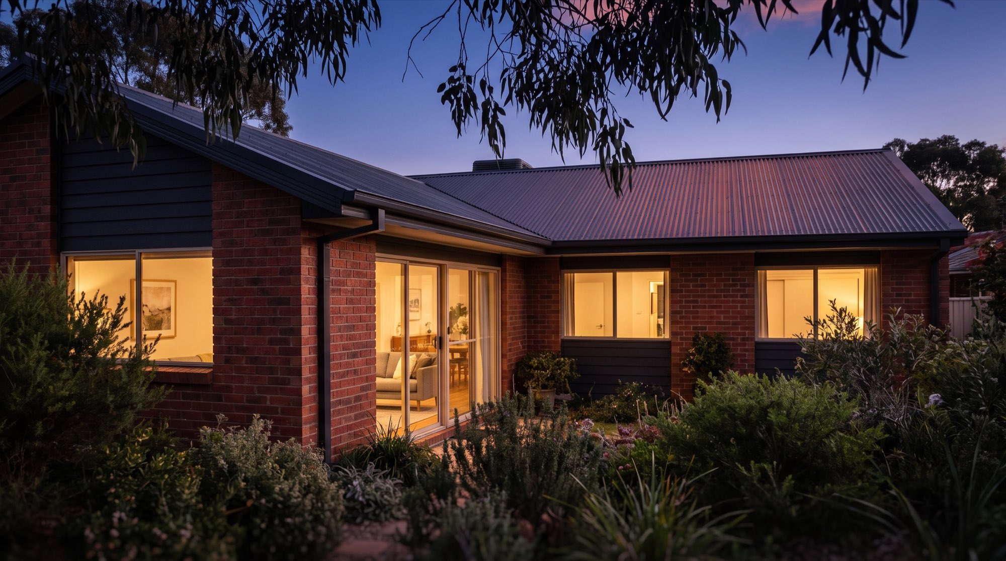 A single-storey brick home at dusk with lit windows and a Colorbond roof