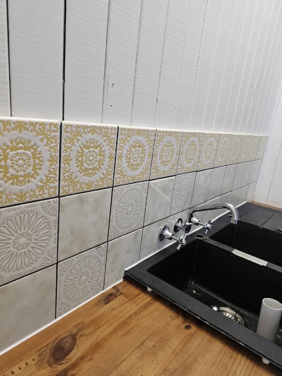 A patterned tiled splashback above a black kitchen sink and mixer tap