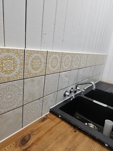 A patterned tiled splashback above a black kitchen sink and mixer tap