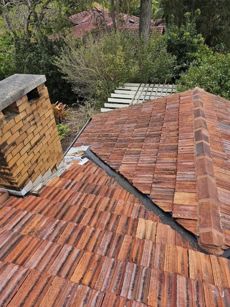A terracotta tiled roof with a brick chimney above a garden