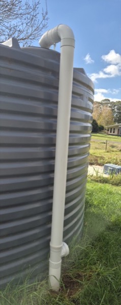 A corrugated rainwater tank with a white downpipe fitted to it