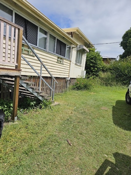 A high-set weatherboard house with timber stairs above a lawn