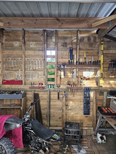 A shed wall hung with hand tools above a workbench