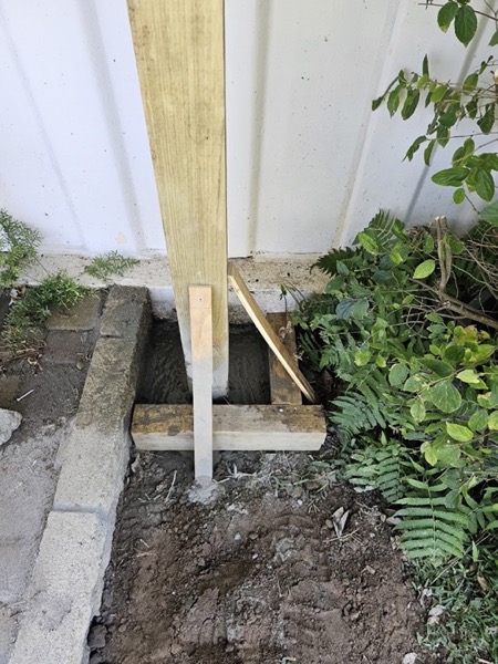 A timber post set into fresh concrete beside a garden path