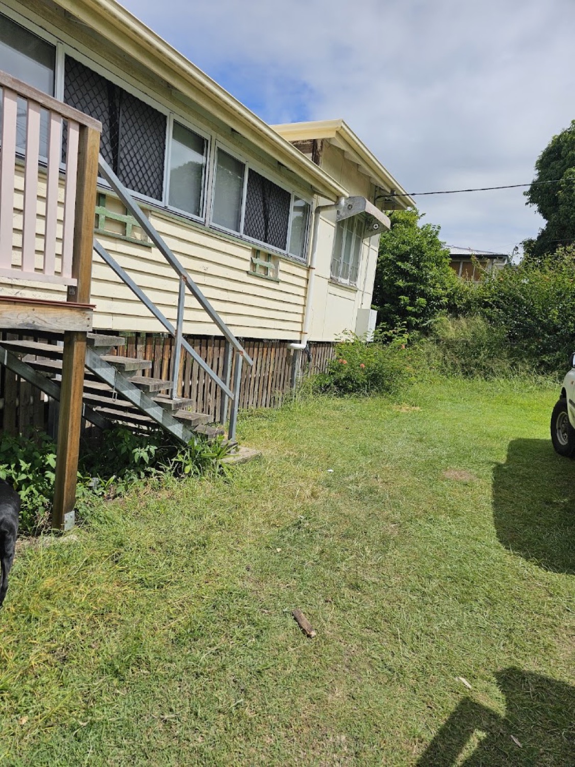 A high-set weatherboard house with timber stairs above a lawn